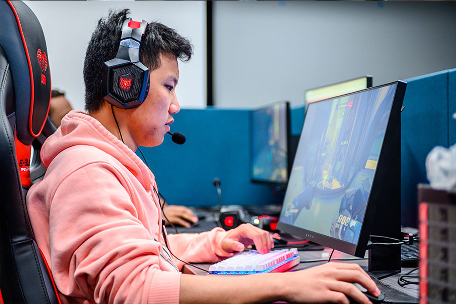 Male student playing video games at a computer with a headset on