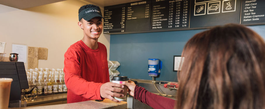 African American student in a red shirt serving coffee at the Lions Den to a female