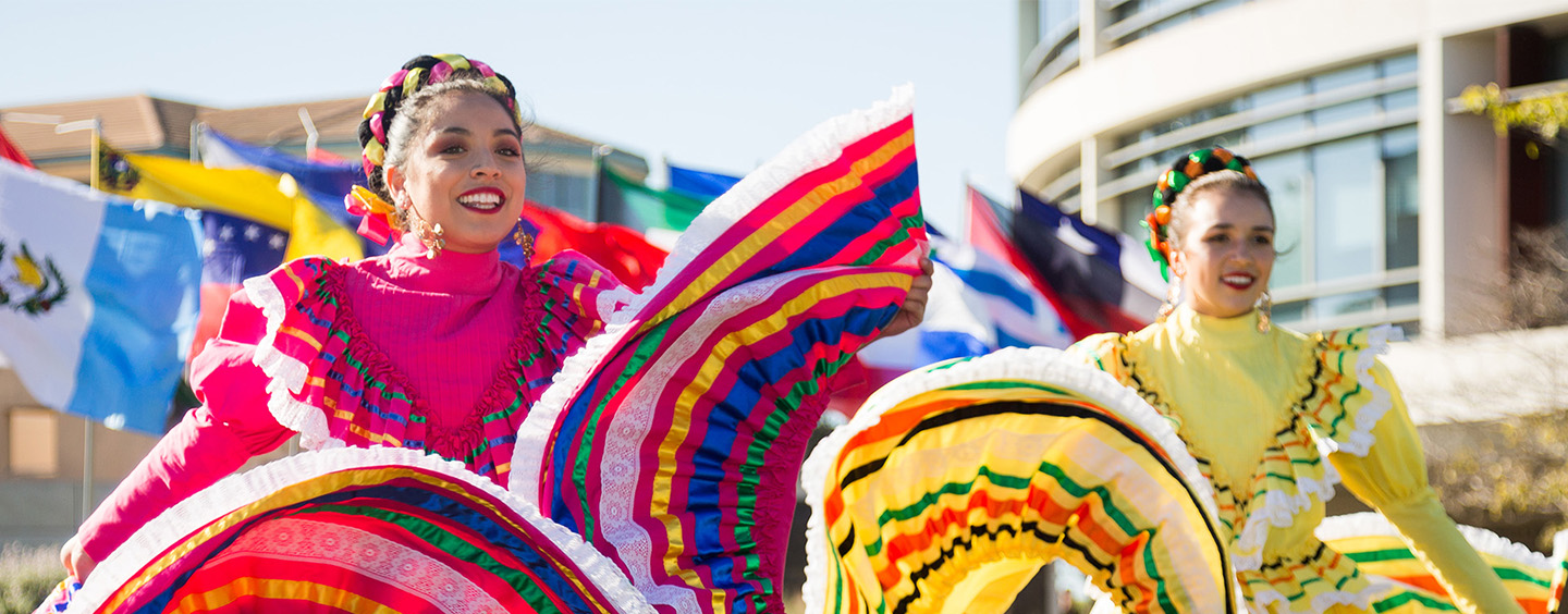 Students performing in Grupo Folklorico de LMU in colorful dresses on the steps outside of the library.