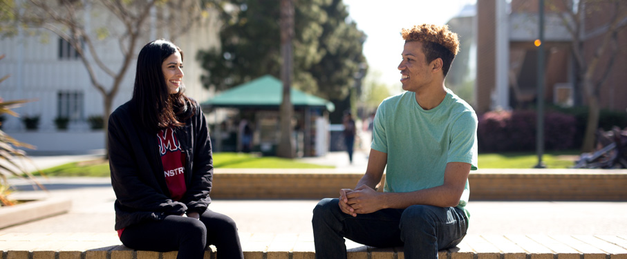 Two students sitting outside at a table having a discussion.