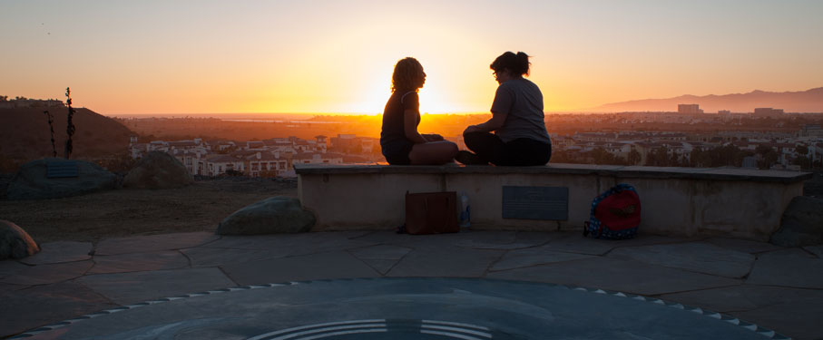 Two students sitting on a bench overlooking the Bluff in front of the sunset 