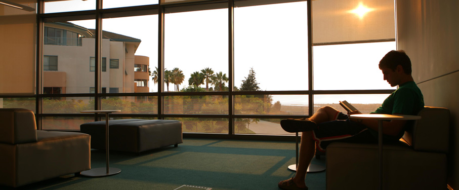 A student reading a book in the library with a view overlooking the bluff.