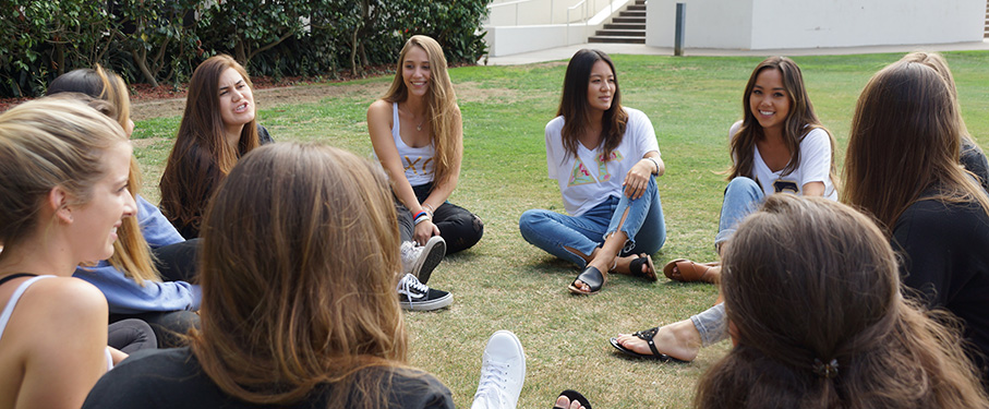 A group of Greek Life students sitting in a circle outside while having a conversation