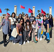 Students pose outside in front of flags on an Alternative Break trip.