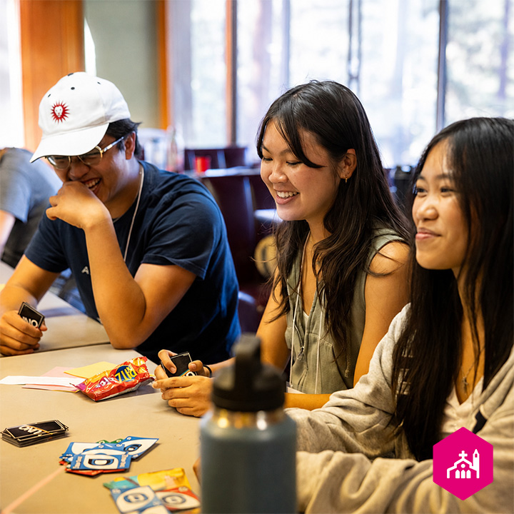 Students sit around a table during a first-year retreat activity, holding game cards and participating in a group discussion