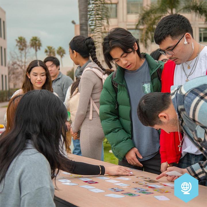 Students gather around an outdoor activity table on campus during a cultural celebration.