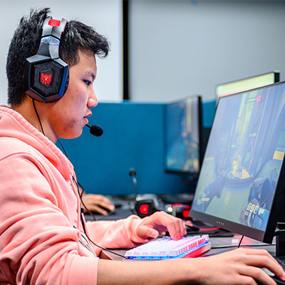 A student with headphones on playing a video game inside the Esports Gaming Center.