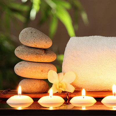 A spa towel, candles and massage stones sit on a table.