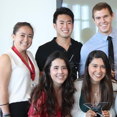 Five students pose for a photo inside where business causal clothes with medals around their necks.
