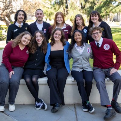 Five students pose outside in front of green trees in their service organization sweaters.
