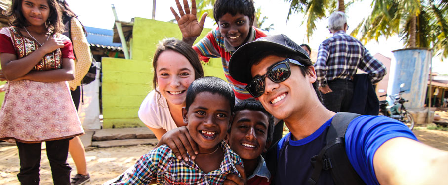 two LMU students smiling with a group of four happy children at their trip location