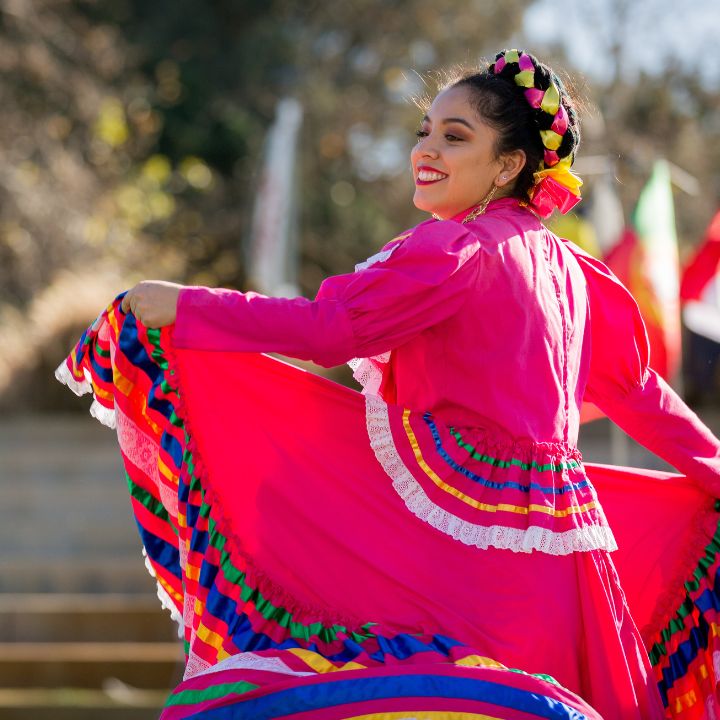 A female student in a pink dress dances on a stage during an international festival on campus.