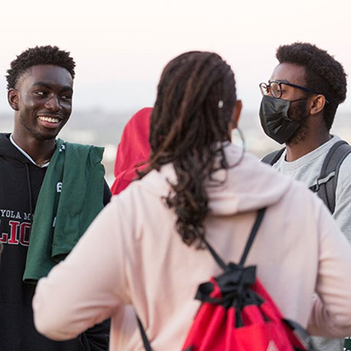 Three students stand outside overlooking the bluff talking by the Mbgoni Spot.