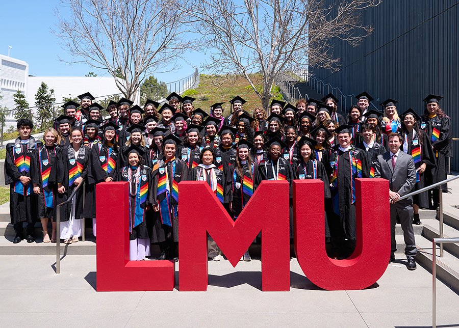 A group shot of students in grad regalia with the red LMU letters in front.