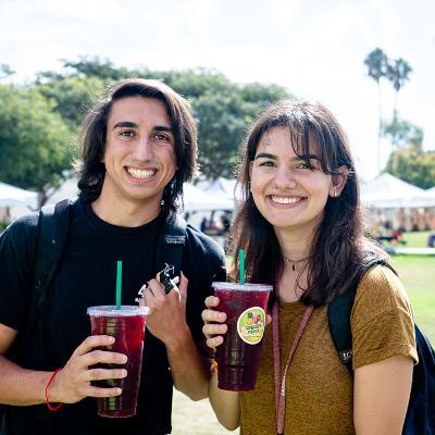 Two students holding iced drinks and smiling at an event in Hannon Field