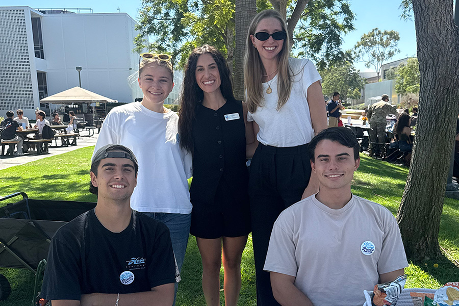 Students and staff pose for a photo outside behind a table.