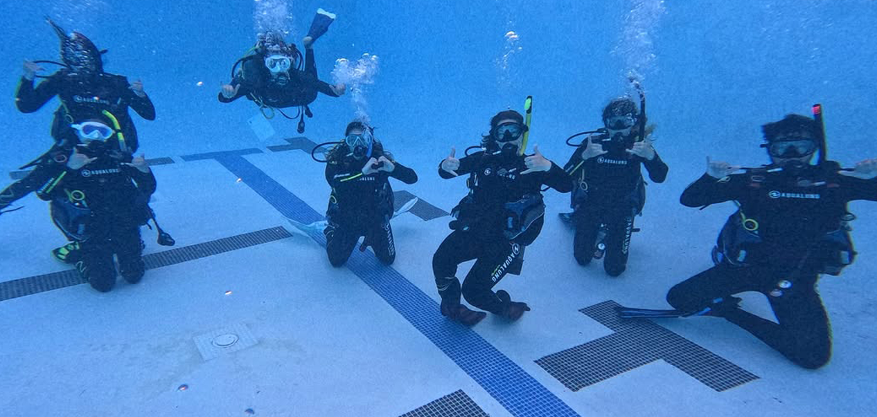 Students and staff in scuba gear underwater in a pool.