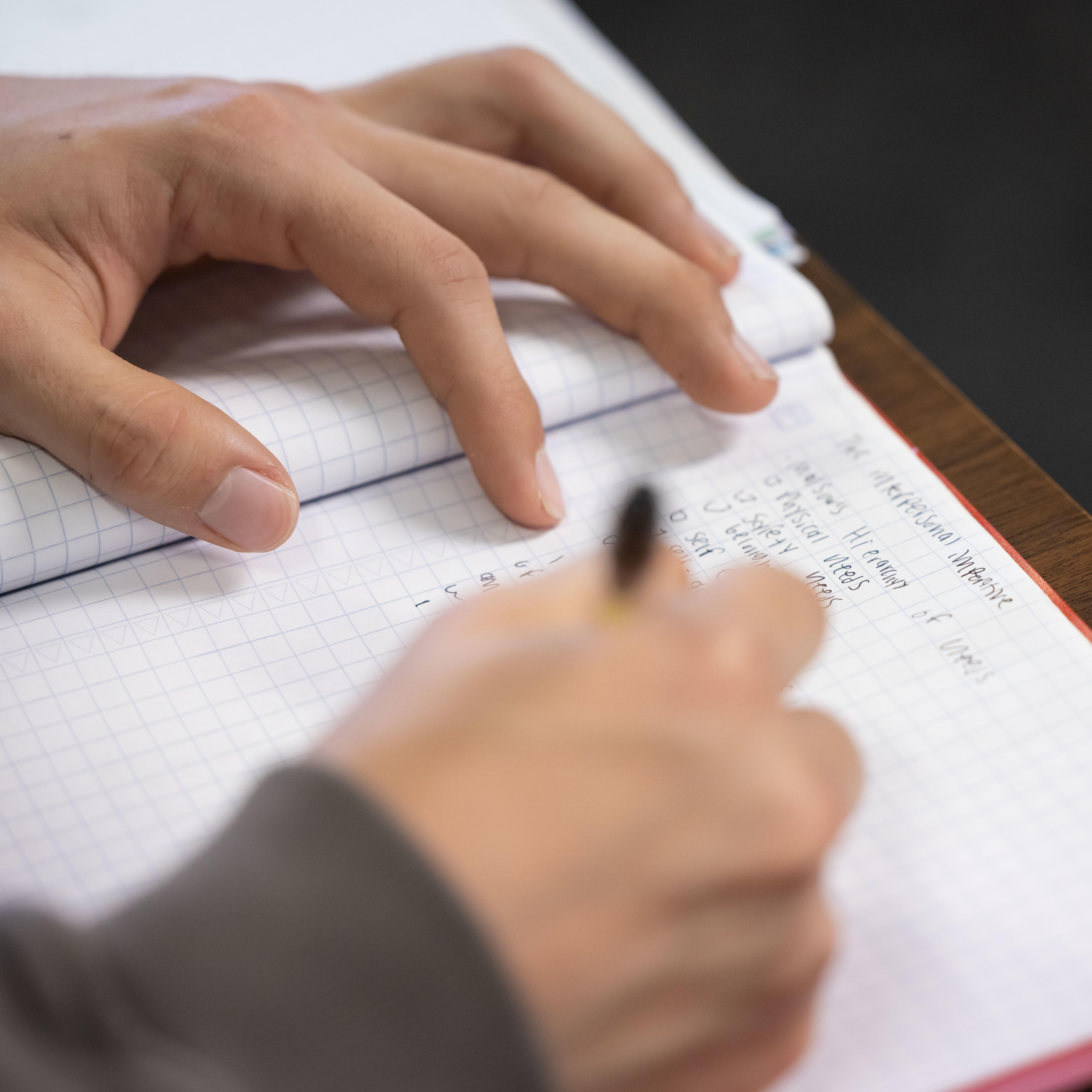 Hands use a pen to write in a notebook.