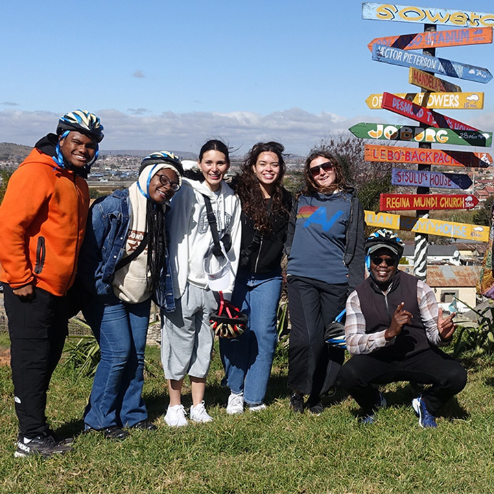 Students and staff pose outside with colorful signs on an immersion trip.
