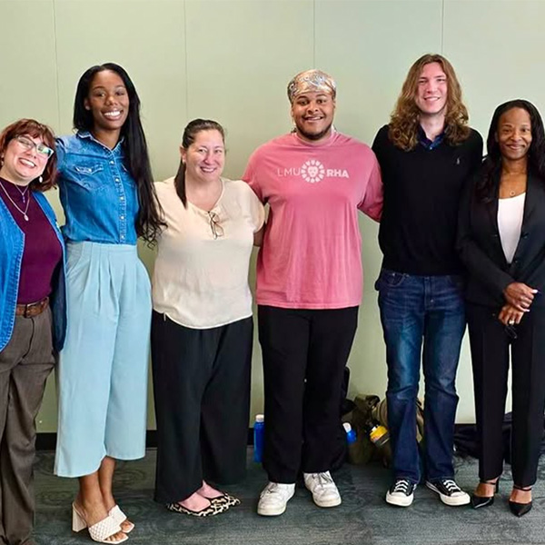 A group of students and two staff members pose inside a conference room after presenting.