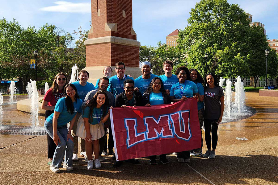 Students, staff, and faculty pose with a red LMU flag.