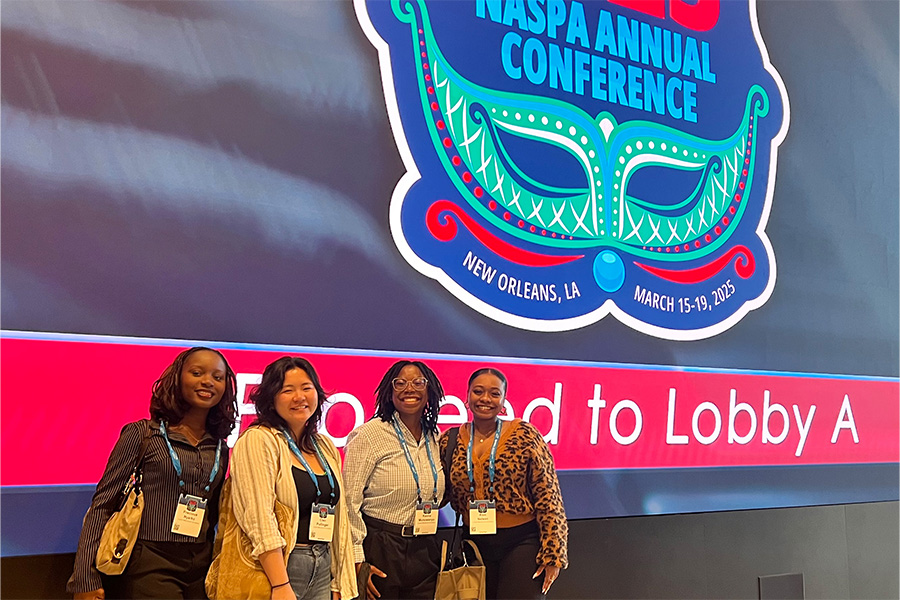 Four students stand in front of a blue and red graphic at a conference in New Orleans.