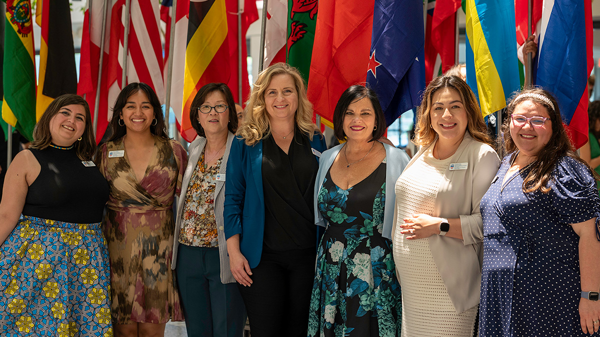 Staff pose in front of international flags during an end of the year grad celebration.