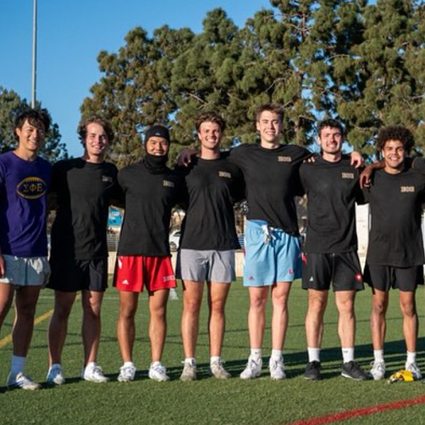 Male students from LMU's fraternities pose for a group photo outside after a flag football game.