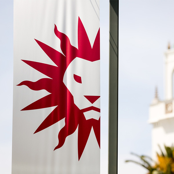The red LMU Spirit Mark on a white flag with a blue sky in the background.