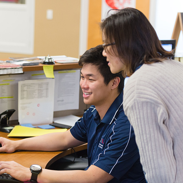 A student employee and a staff member work together at a fronk desk to review something at a computer.