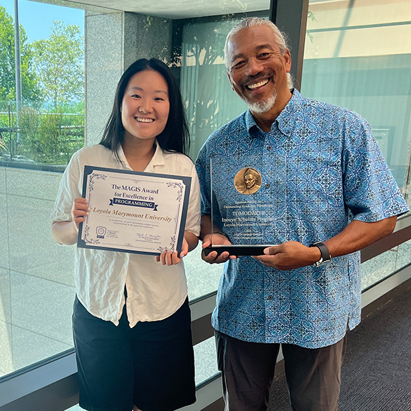 Two staff members stand holding awards for the Tomodachi Scholars Program.