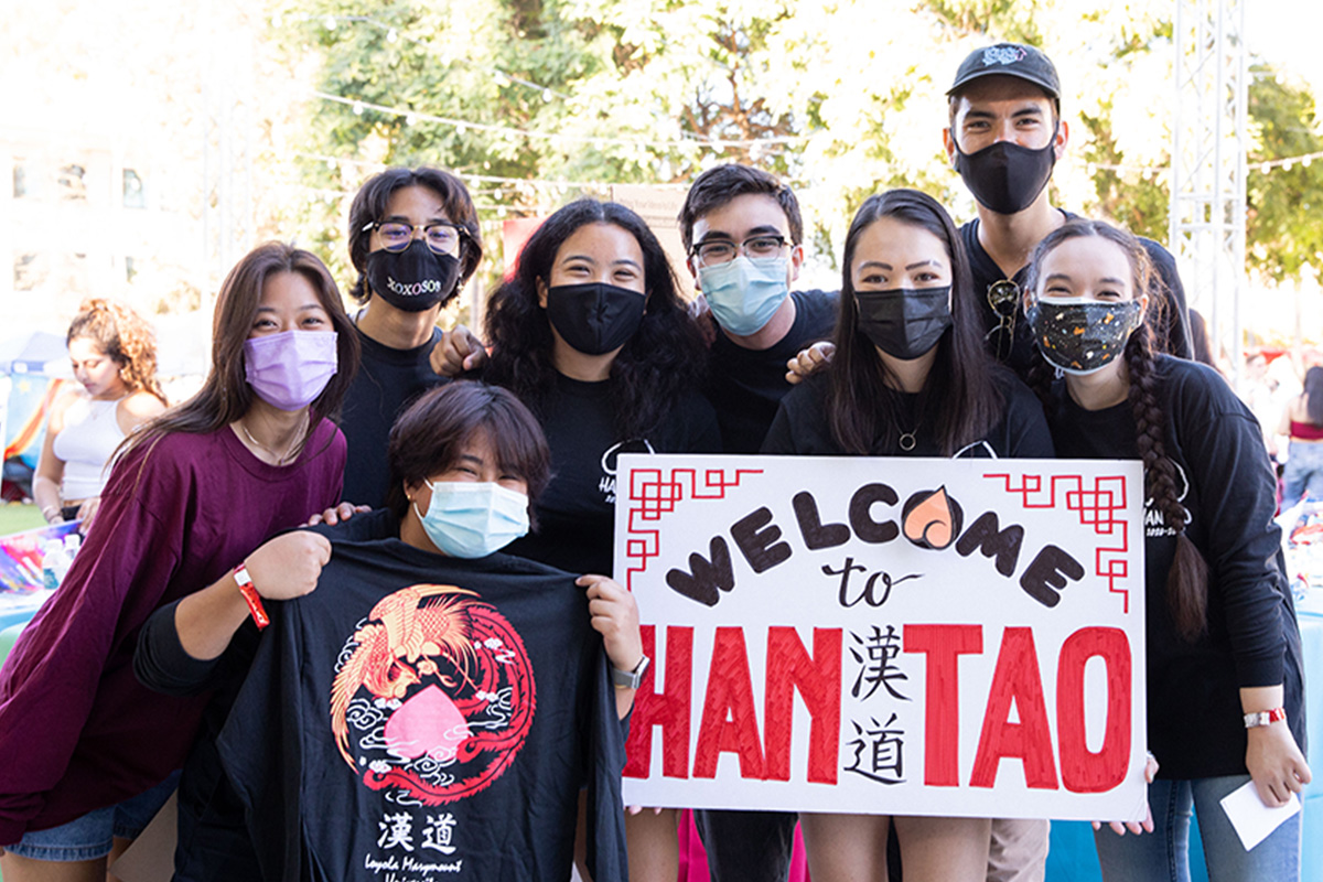 A group of students from the Han Tao RSO hold a t-shirt and sign outside.