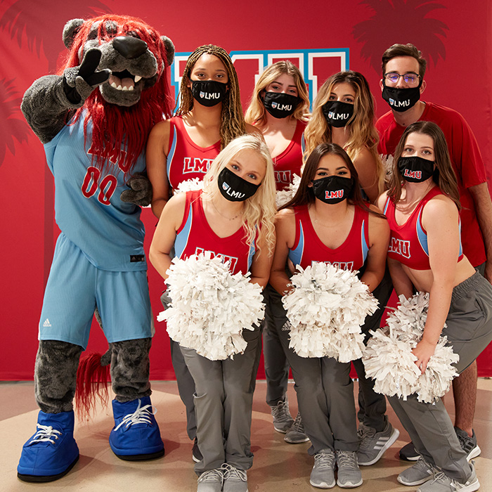 Spirit squad and the Iggy mascot gathered in front of an LMU banner at an event.