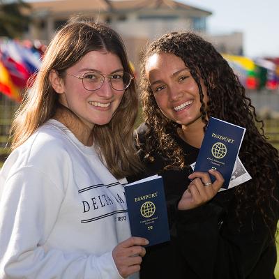 Two students stand outside the library holding passports.