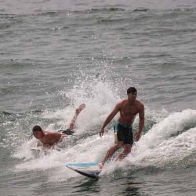 Two male students in black wet suits out on the ocean surfing.