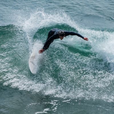 A male student in a black wet suit surfing in the ocean.
