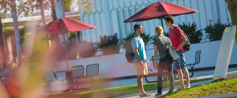 Three students talking together outside by the lunch benches.