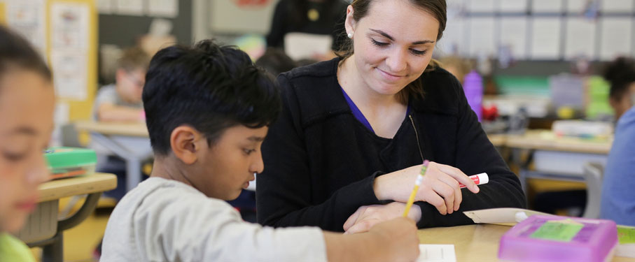 a woman helping a child in a classroom