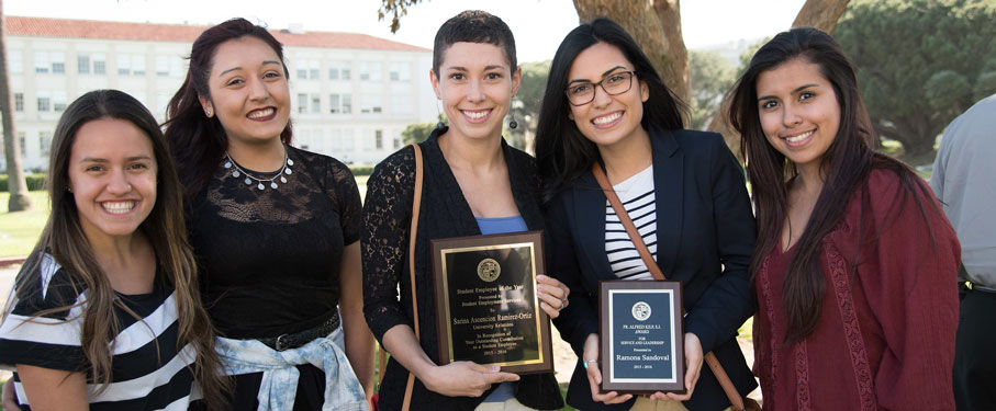 five students smiling into the camera and two of them holding award plaques