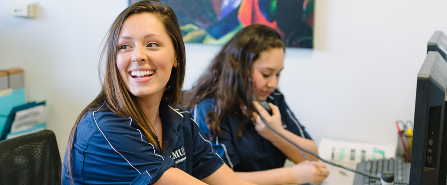 student smiling to the camera another student on the phone