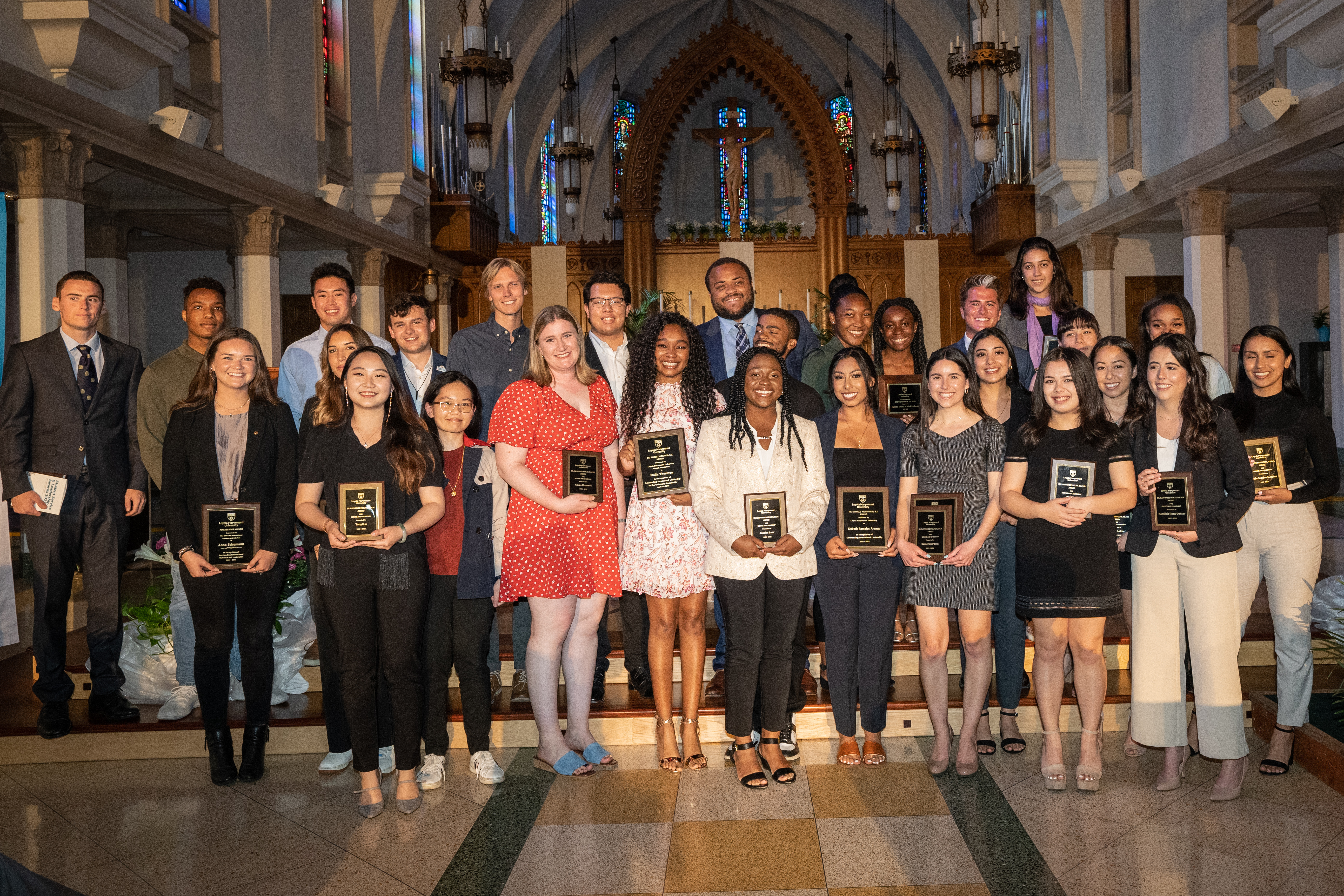 Senior students are standing inside the chapel on the altar steps smiling and holding award plaques.