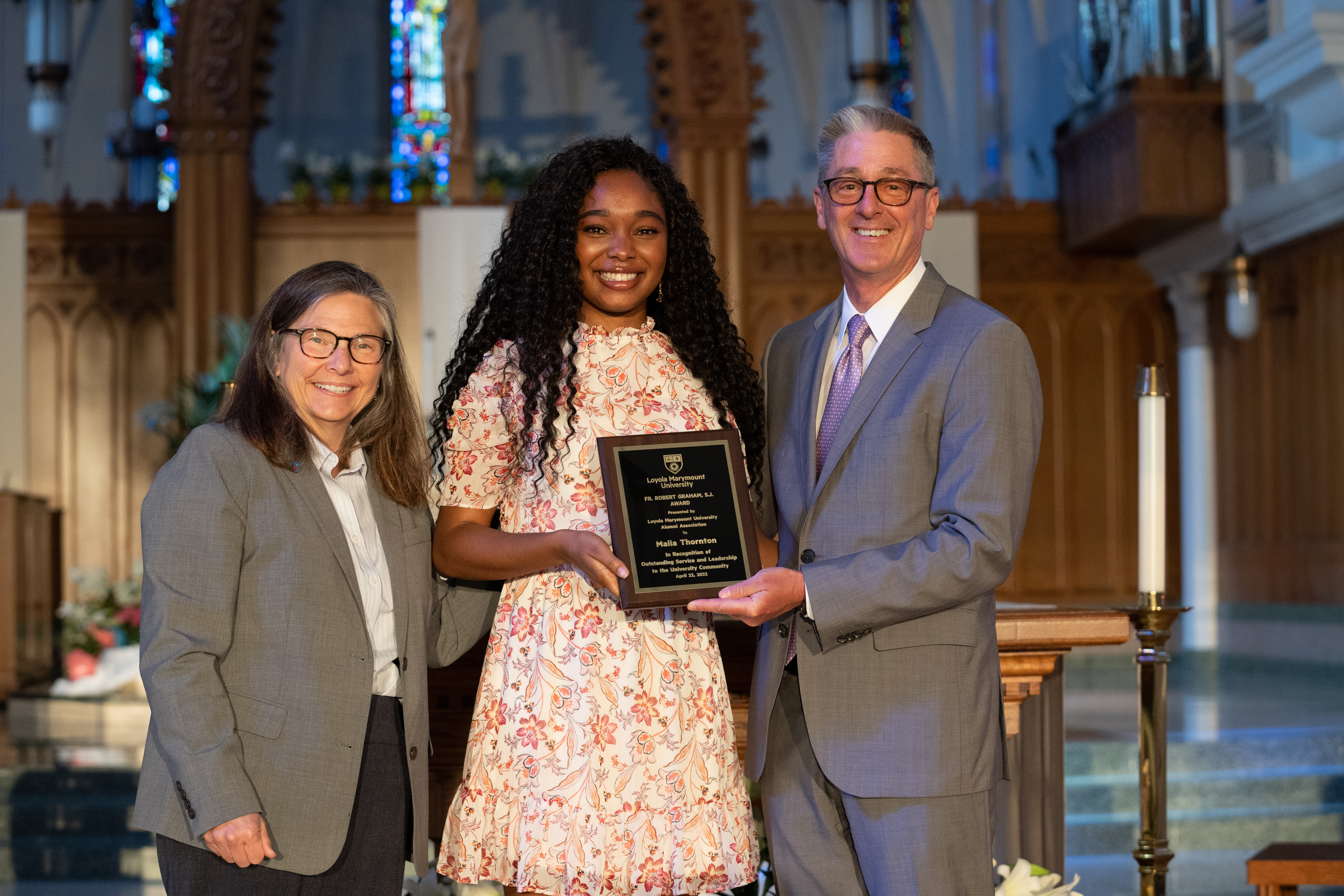 Dean Mangione, President Snyder and Graham Recipient Malia Thornton are standing on the alter smiling and holding a plaque.