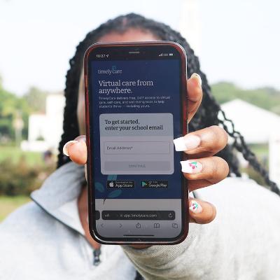 Student holding a phone with TimelyCare teletherapy app on the screen.
