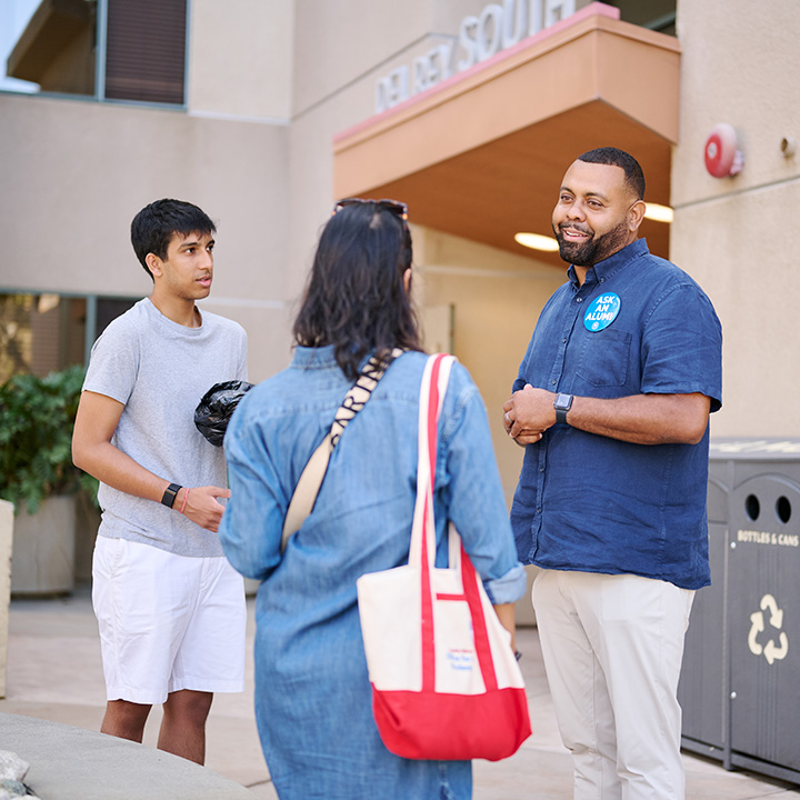 Three people converse outside a residential campus building during move-in