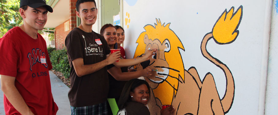 Five students painting a mural of a lion at a local school