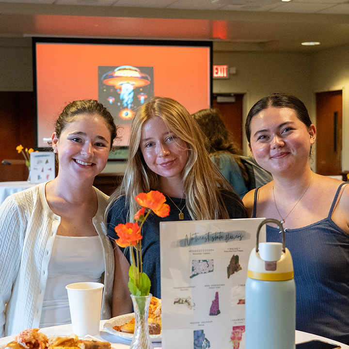 Three students sit together at a round table during an LMU Hometown Pride event