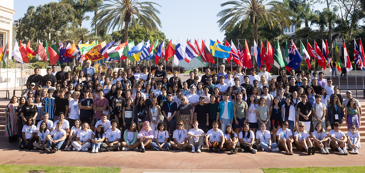 Students and staff pose outside in front of international flags for international student orientation